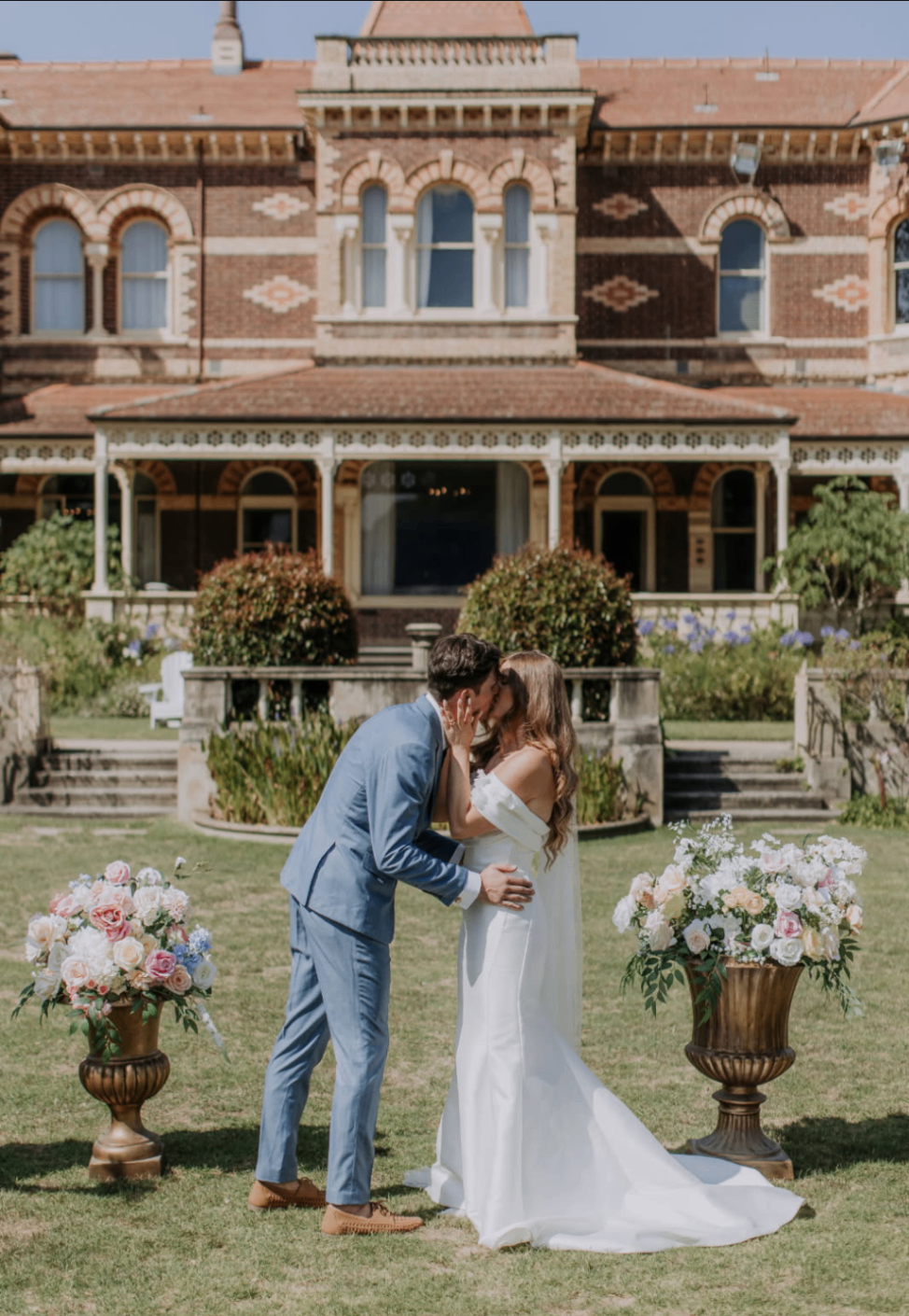 Amber and Steven sharing a kiss between floral urns in front of the venue