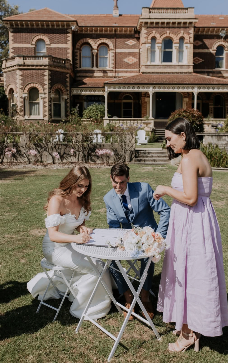 Amber and Steven signing wedding documents at a white outdoor setting