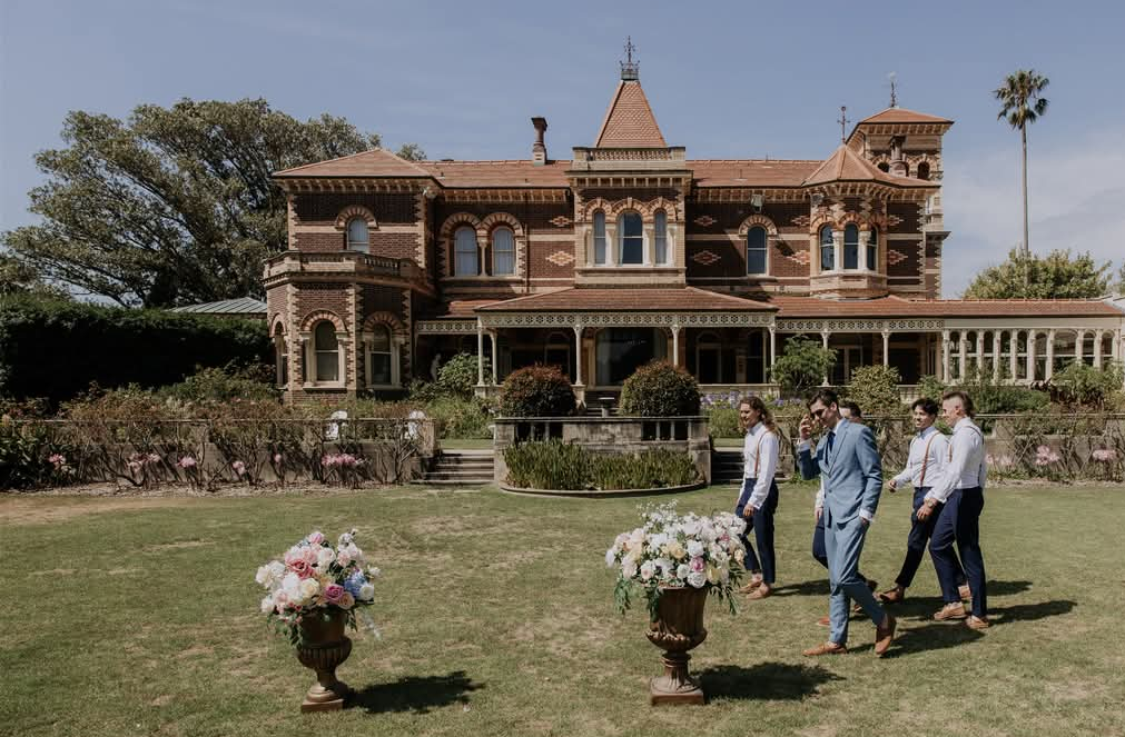 Groomsmen walking across the lawn with floral urn styling in front of the house