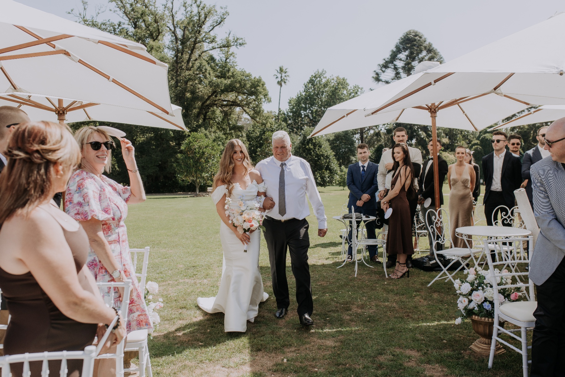 Amber walking down the aisle with guests seated beside white ceremony furniture